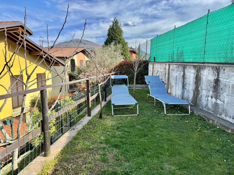 backyard with green grass, 2 lounge chairs, wooden fence, small yellow house in background