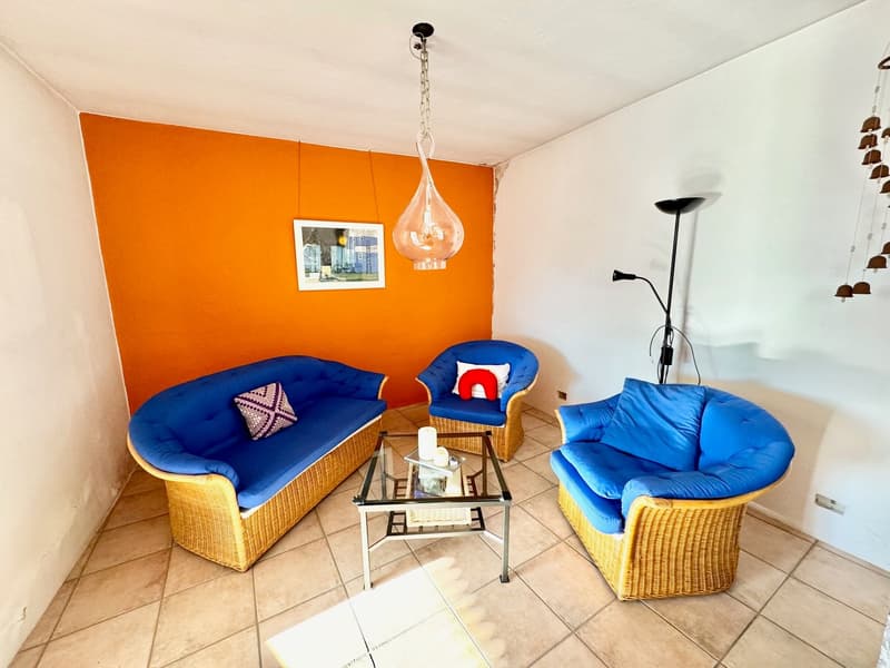 Bright and colorful living room with orange walls, blue and yellow wicker furniture, glass coffee table, and a pendant light fixture