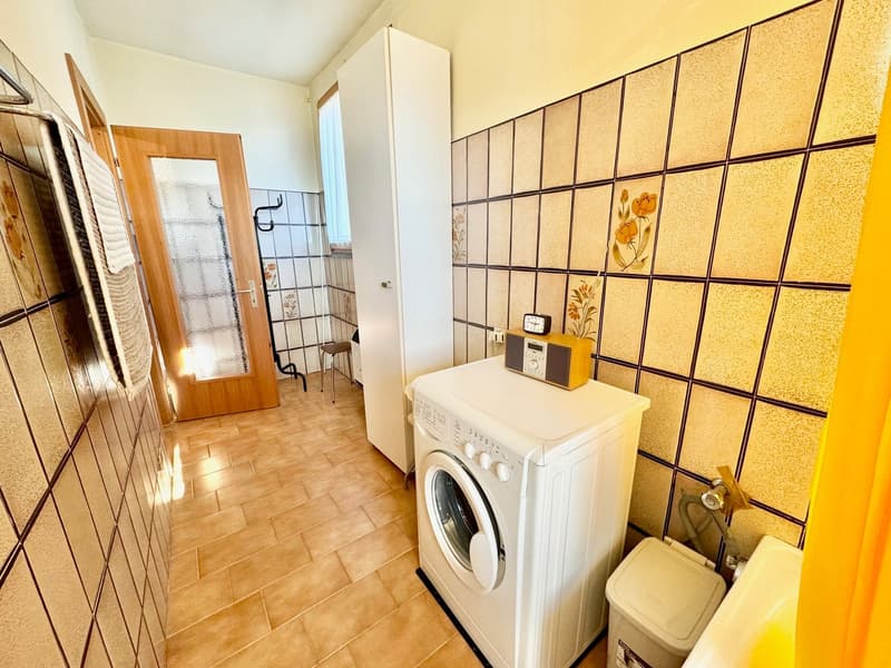 Laundry room with tiled walls, washing machine, and trash bin.
