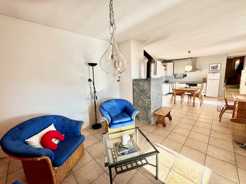 Blue armchairs, coffee table with candles, floor lamp, stone table, tiled floor, kitchen with white appliances, dining table, shelves with picture frames