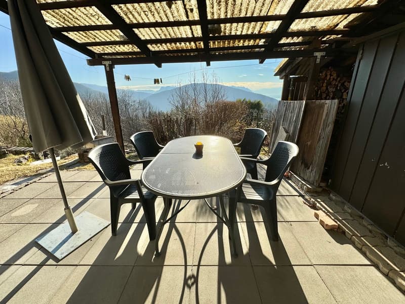 Outdoor dining area with a table and chairs, covered by a pergola with a view of mountains
