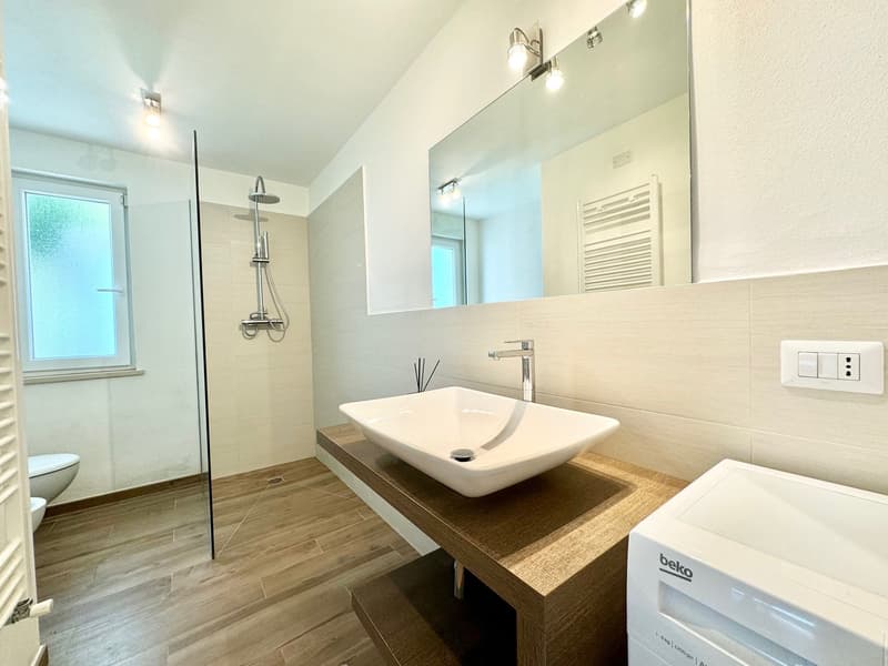 Modern bathroom with white walls, wood-look tile flooring, a vessel sink on a wooden vanity, a shower with glass enclosure, and a towel warmer on the wall.