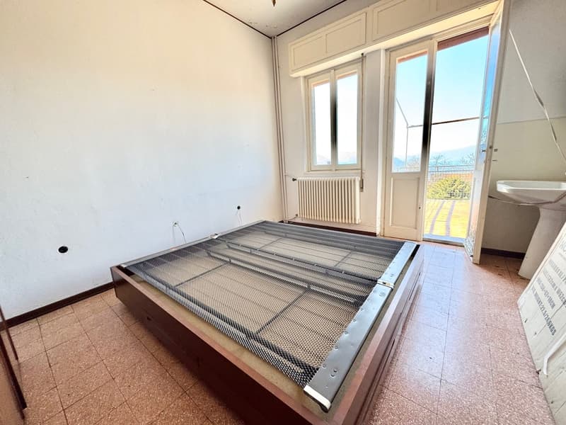 Spacious bedroom with large windows, white walls, and a wooden bed frame with a metal mesh platform.