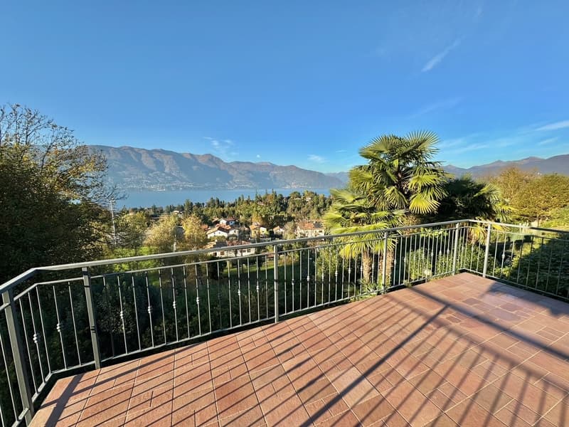 Spacious balcony with a panoramic view of the lake and mountains, surrounded by lush greenery and palm trees