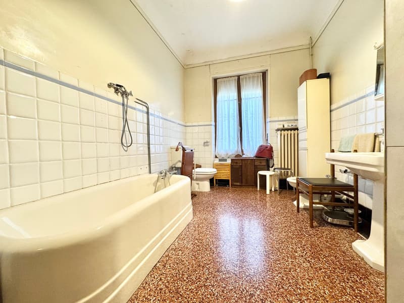 Large bathroom with a bathtub, tiled walls, wooden furniture, and a washing machine.