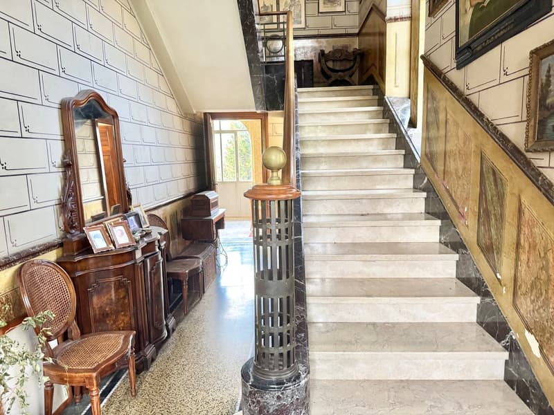 Ornate marble staircase, antique furniture and decor, framed artwork on the walls, decorative column in the entryway