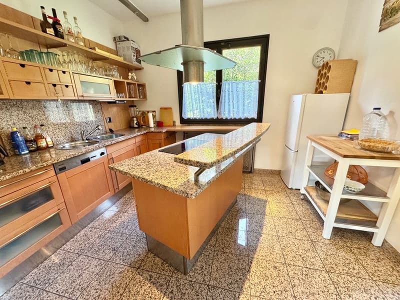 Kitchen with modern appliances, central island, granite countertops, white refrigerator, white cabinets, modern sink, gas stove, wine rack.