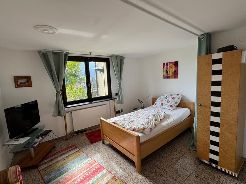 bedroom with bed, TV, cabinet, carpet, and window with curtains