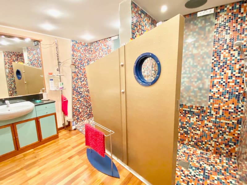 tiled walls, wooden floor, a sink, a shower, a mirror, colorful tiles