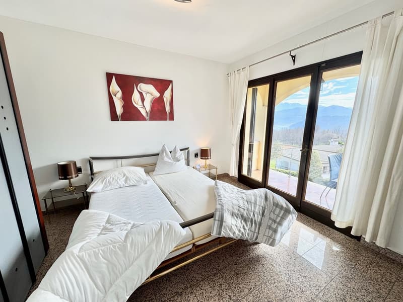bedroom with double bed, bedside lamps, sliding glass doors leading to balcony, artwork, tiled floor
