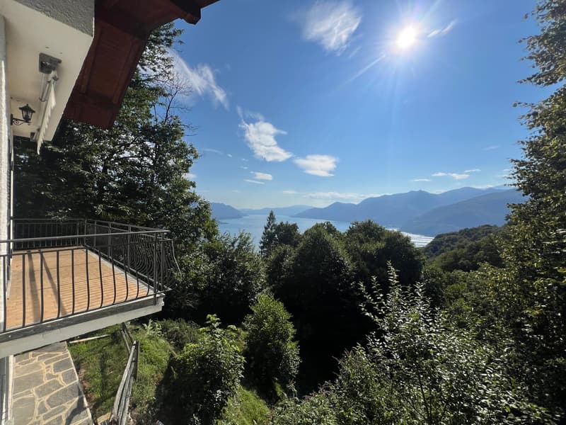 House with balcony, scenic view of the mountain and water body, bright sunny day, surrounded by greenery
