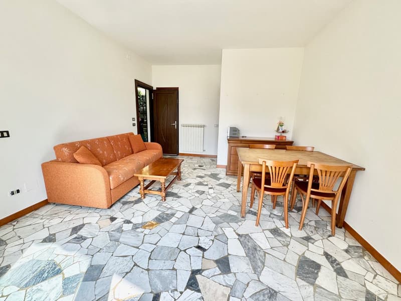 Living room with stone floor, orange couch, wooden coffee table, wooden dining table with chairs, white walls, wooden door, white radiator