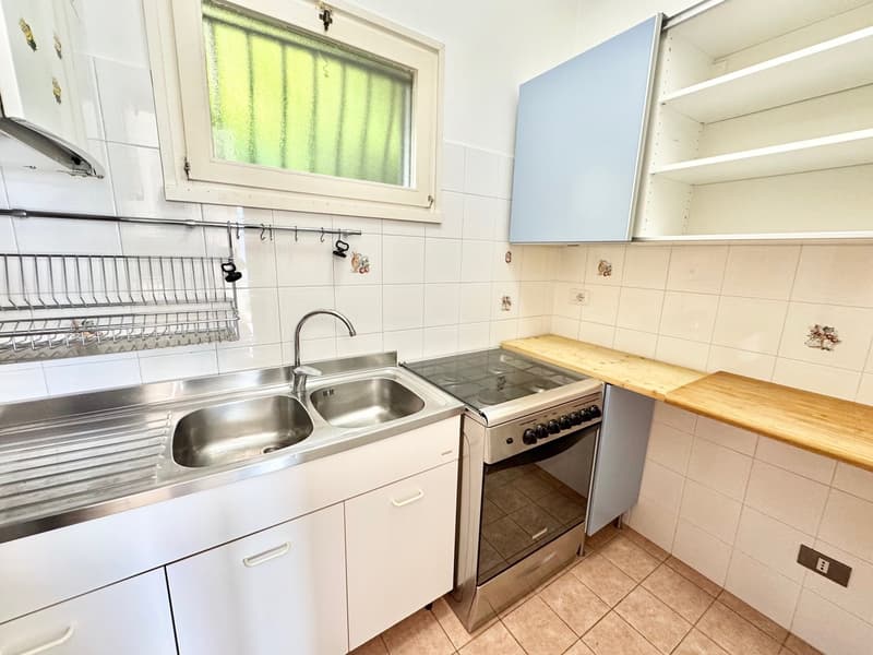 white cabinets, stainless steel sink, gas stove, wooden countertop, white tiles, window with curtain