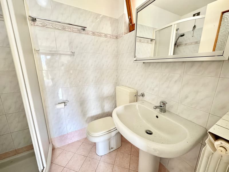 White tiled walls and floor, toilet, sink, shower, mirror, showerhead