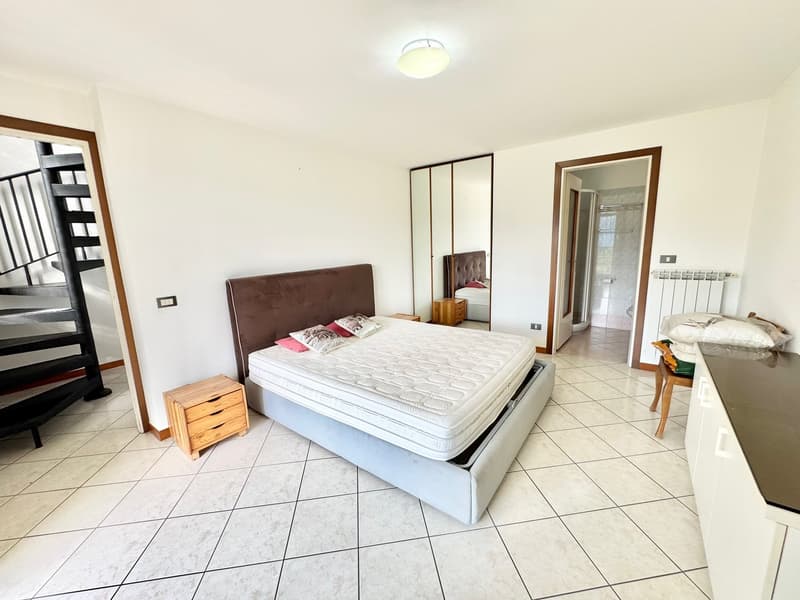 Large bed with pillows, wooden nightstand, wooden chair, radiator, staircase, mirror