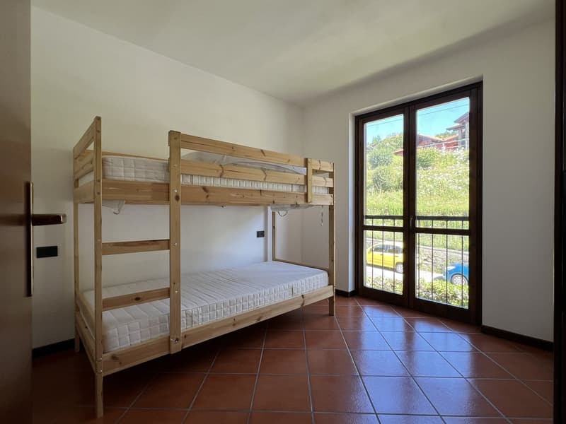 Wooden bunk beds, glass sliding door with metal grill, white walls, tiled floor, power outlet