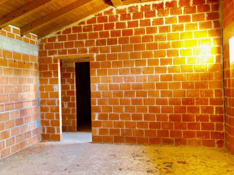 Empty room with brick walls, wooden ceiling, small window, and doorway.