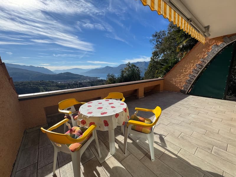 A terrace with a table and chairs, surrounded by a view of mountains and a lake.