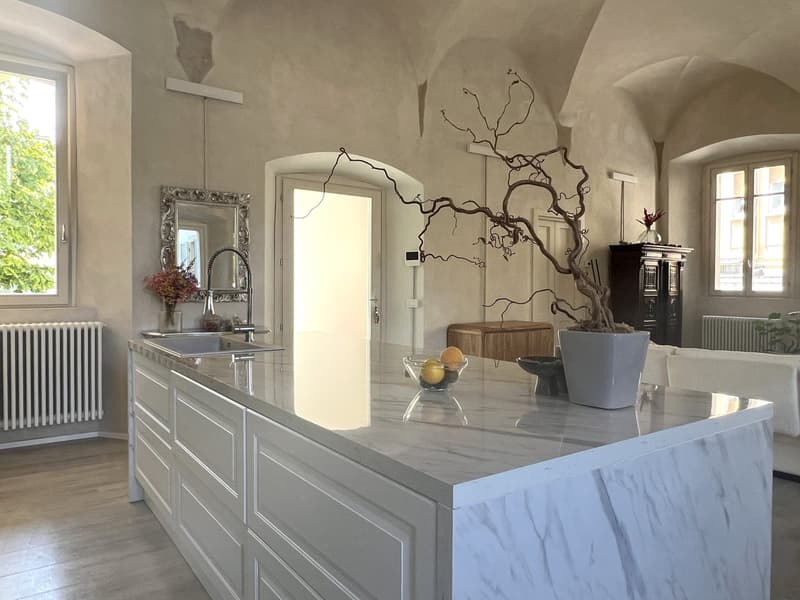 Kitchen: large marble island, stainless steel sink, silver faucet, white wooden cabinets, radiator, mirror