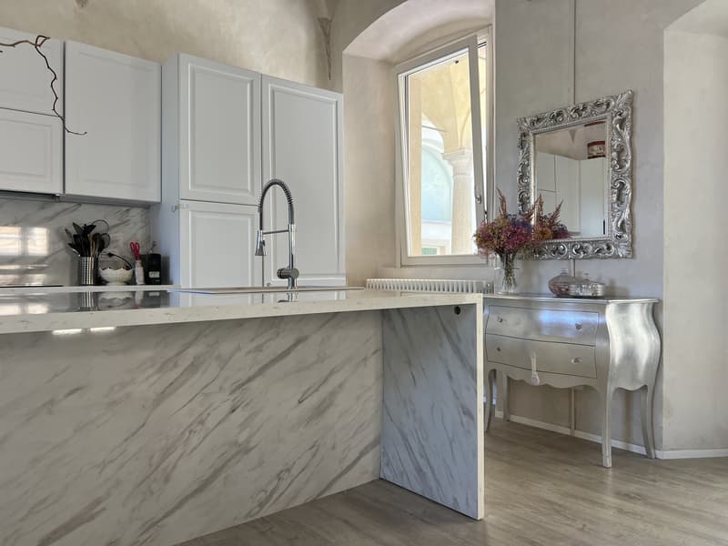 modern kitchen with marble counter, white cabinets, central island, silver cabinet, open window, faucet, radiator, mirror with ornate frame