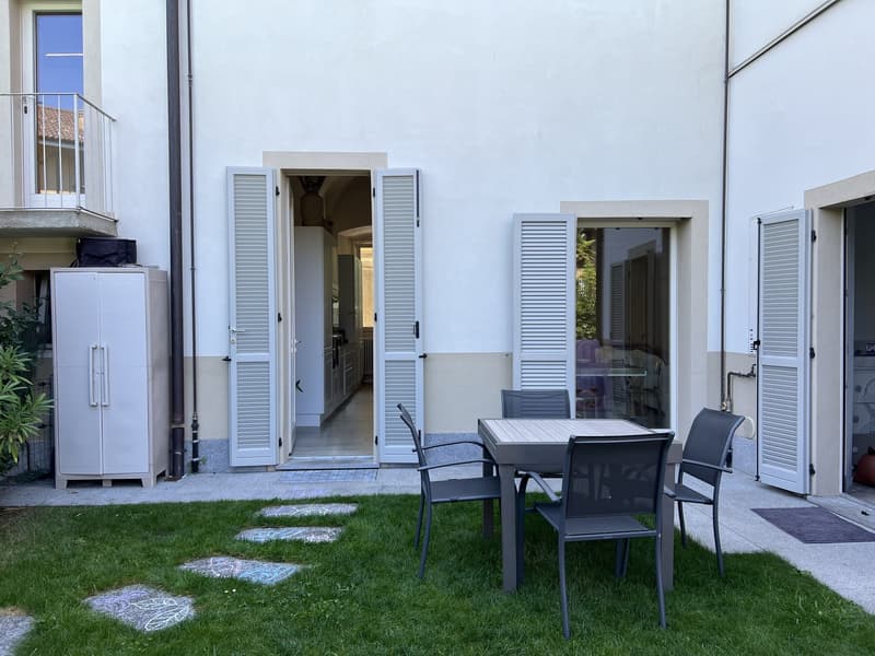 Exterior of a white house, balcony with metal railing, open windows, garden table and chairs, side door entrance