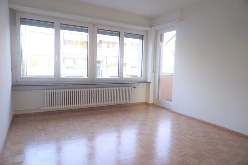 Empty room with large windows, wooden floor, radiator, sliding door