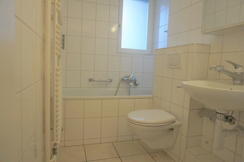 modern bathroom with bathtub, toilet, sink, and wall-mounted radiator