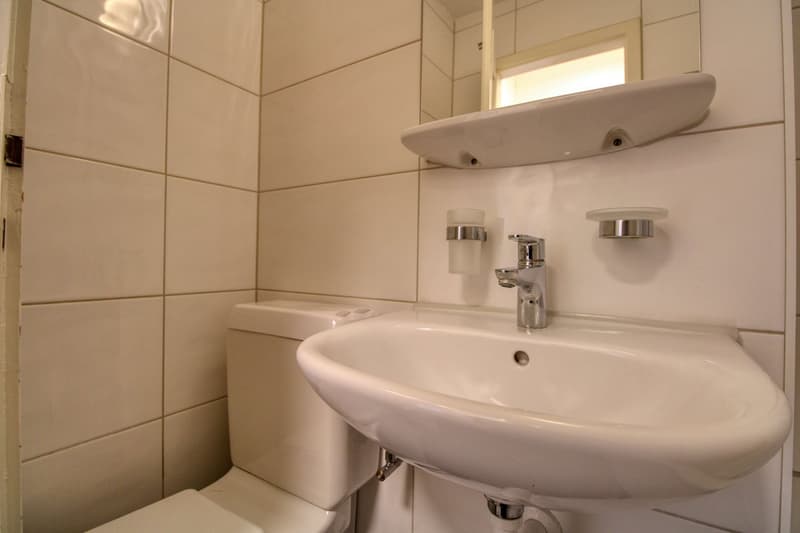Bathroom with white tiles, white toilet, white sink, silver faucet, mirror above sink