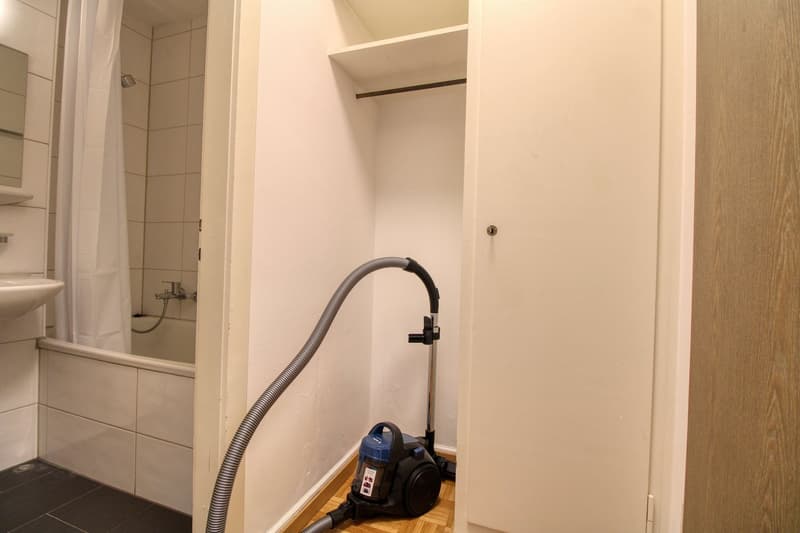Bathroom with bathtub, shower, sink, mirror, and a vacuum cleaner in the corner