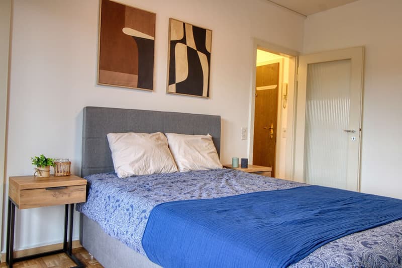 Bedroom with bed, nightstands, paintings, and a door.