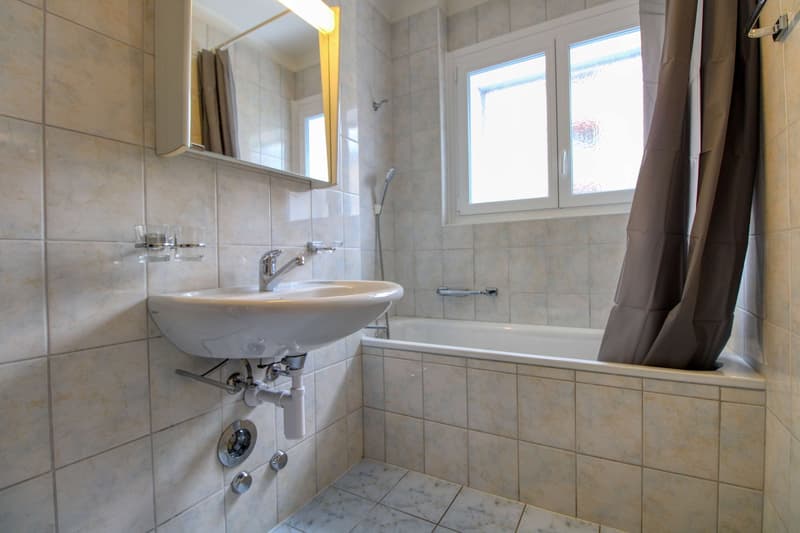 Bathroom with white tiles, white sink, bathtub, shower, mirror, and window.