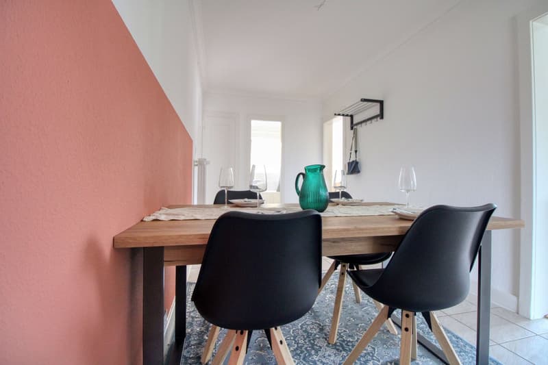 dining table with 4 chairs, white and pink walls, wooden floor, green jug, wine glasses, plates