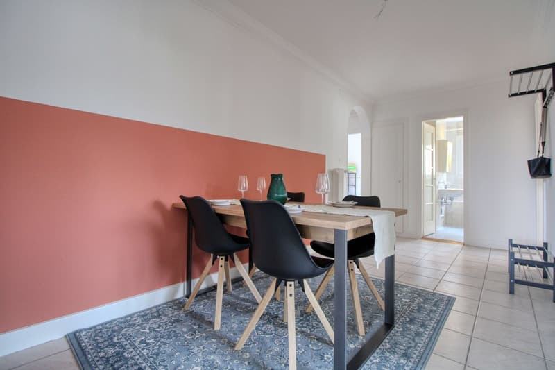 Dining room with a wooden table, black chairs, a pink wall, and a blue rug