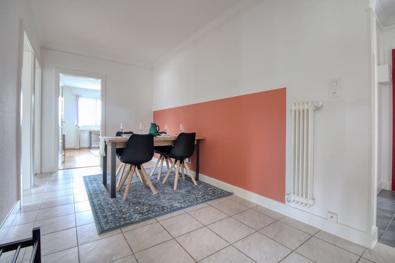 modern dining area with a wooden table, four black chairs, a red accent wall, a white radiator, and a white ceiling