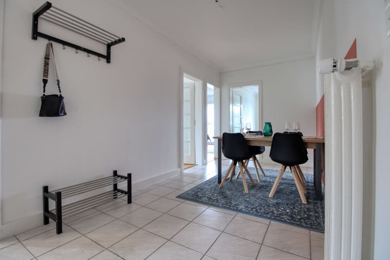 Dining room with a wooden table, black chairs, a rug, and a handbag on a wall rack.