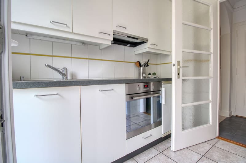 white kitchen with tile flooring, built-in oven, sink with faucet, cabinet drawers, countertop, open door