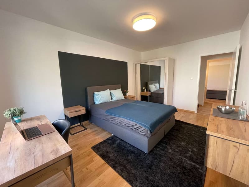Bedroom with bed, desk, chair, nightstands, mirror, carpet, and potted plant