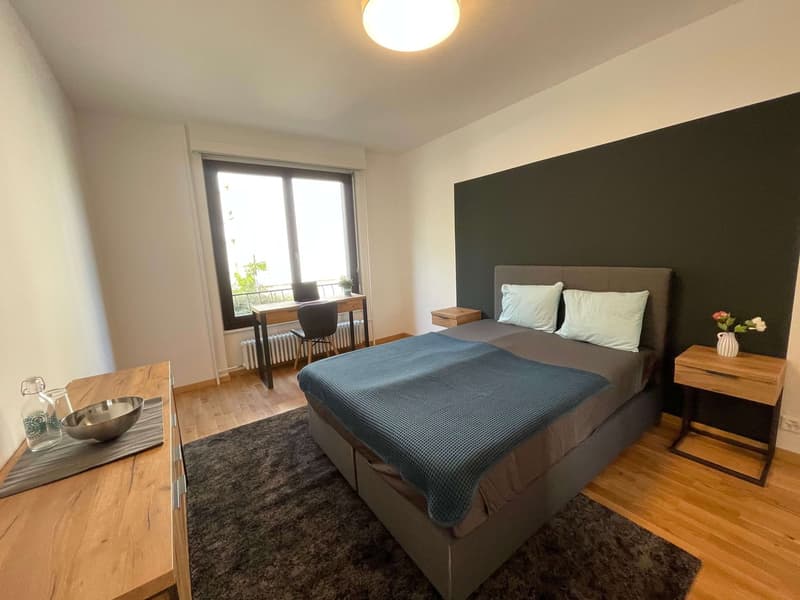 Bedroom with bed, desk, chair, radiator, carpet, nightstands, flowers, bowl, bottle, lamp