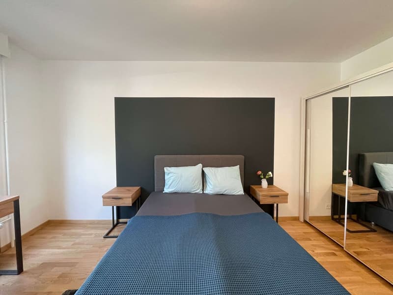 Bedroom with a bed, two nightstands, a gray headboard, and a gray wall. The room has wooden floors and white walls.