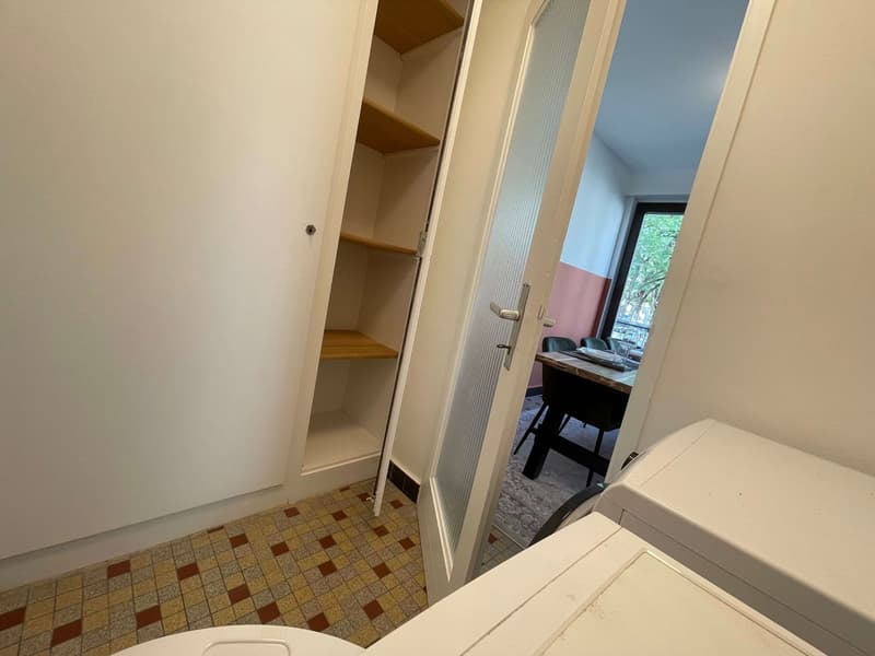 A small room with a white washing machine, a wooden cabinet with shelves, and a tiled floor.
