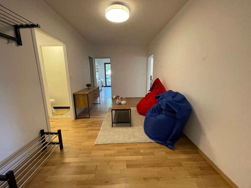 Empty room with wooden floor, white walls, a wooden cabinet, a rug, a coffee table, and bean bags