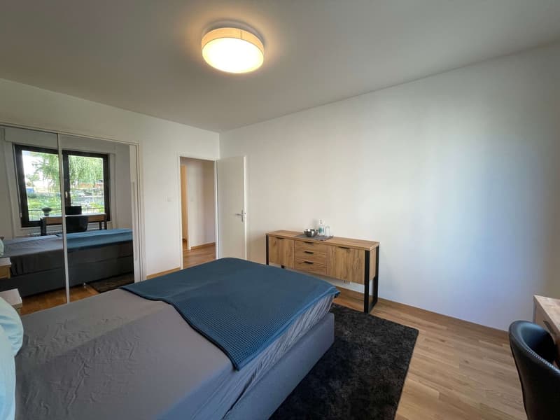 Bedroom with bed, wooden cabinet, desk, chair, and a view of the outside through the glass door.