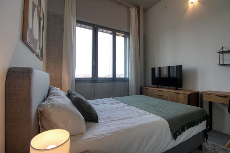 double bed, pillows, blanket, lamp, TV, wooden cabinet, desk, shelves, window with curtains