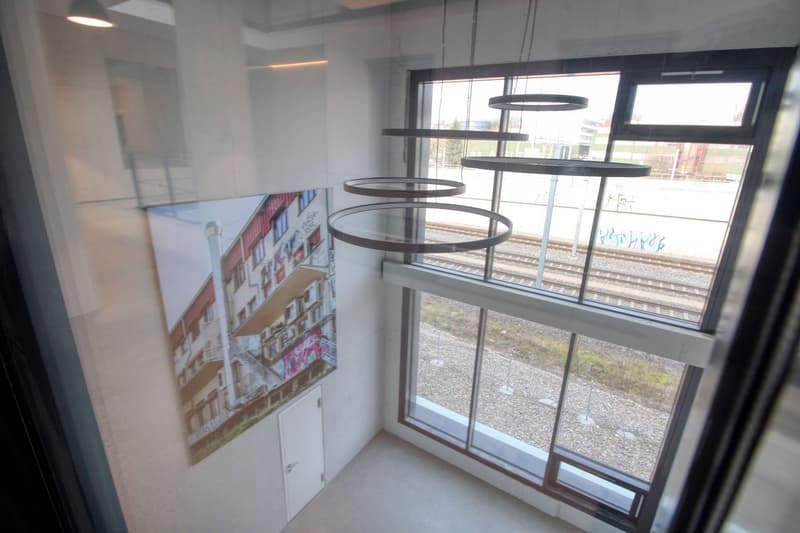 modern interior, large windows, circular light fixture, artwork on wall, view of train tracks