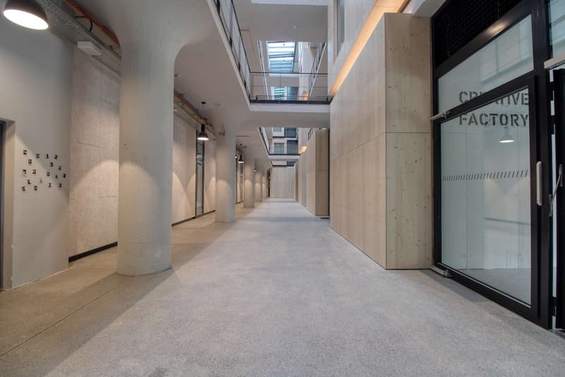 Empty hallway with concrete floor, white walls, and glass doors. There are two levels with a balcony and a skylight.