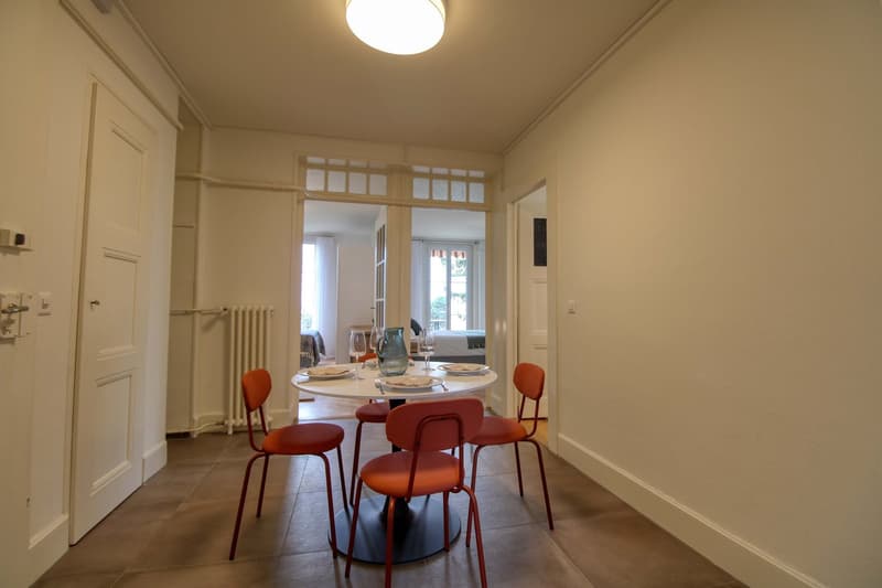 Dining area with a round table and four chairs, white walls, tiled floor, ceiling light, open door leading to a bedroom