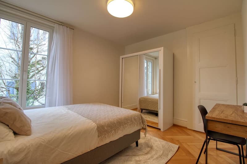 Bedroom with bed, desk, chair, mirror, rug, and window with curtains