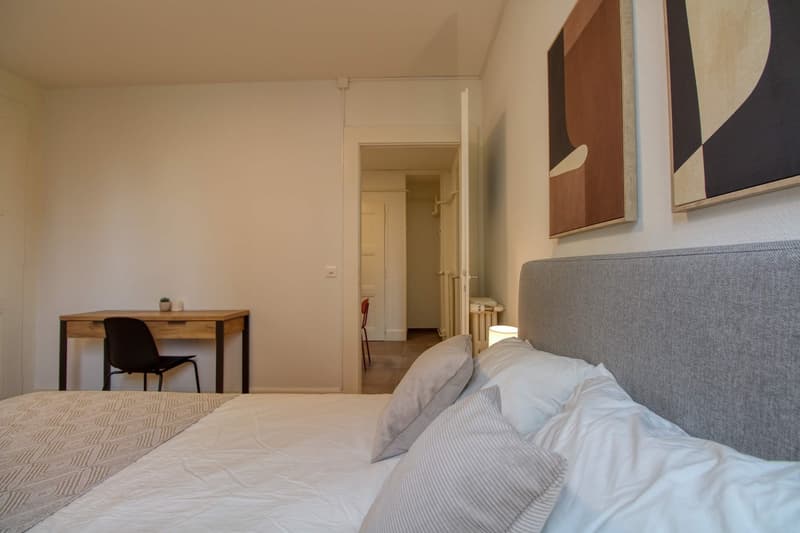 Bedroom with bed, desk, chair, and paintings on the wall