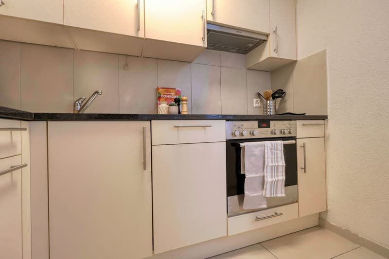modern kitchen, white cabinets, black countertops, stainless steel appliances, gas stove, oven, sink, faucet, white tiled floor