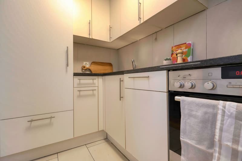 modern kitchen with white cabinets, tiled floor, countertop, oven, sink, towel, chopping board, and a plant